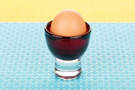Single brown egg in eggcup on blue tablemat.の写真素材