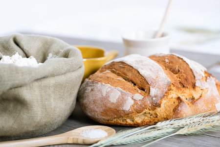 Homemade sourdough bread with flower, sourdough starter, salt, water and ears of wheat on a rustic table.の写真素材