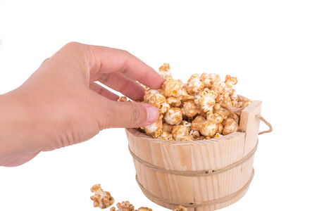 Hand picking caramel popcorn filled in a wood basket on white backgroundの写真素材