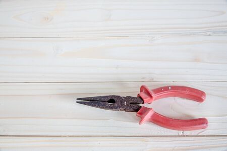 A pair of rusty needle nosed pliers with red handles on wooden backgroundの写真素材