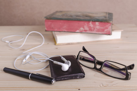 brown wallet, spectacles,earphones, pen, stack of old big books vintage style, selective focus on earphonesの写真素材