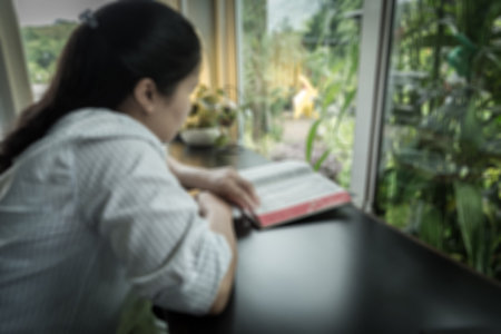 blurred image of a woman reading the holy bible in the church for religion background
