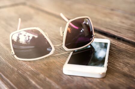 smartphone and sunglasses on wooden table, View of glasses and a smartphone on wood desk - vintage effect styleの写真素材