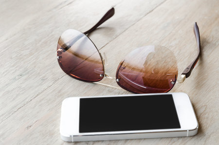 smartphone and tinted sunglasses  on wooden background - with selective focus