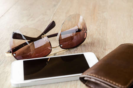 a set of tinted sunglasses and smartphone, leather wallet on wooden background-with selective focusの写真素材