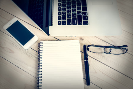 Blank business laptop, pen, note and glasses on wooden table, Vintage filters