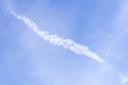 Airplane contrail against beautiful blue sky with delicate cloudsの写真素材