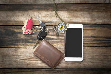 Top view of digital smart phone lying on dark wood table with keys, tie wallet, pocket watch :...