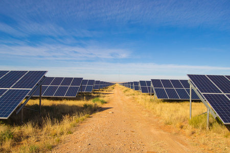 Solar panel rows on solar farm with blue sky and gravel road