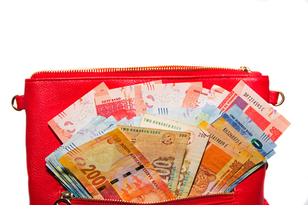 Rand banknotes in a red handbag isolated on white backgroundの写真素材