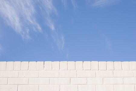 Blue sky and white brick wall background with light clouds on a suuny dayの写真素材