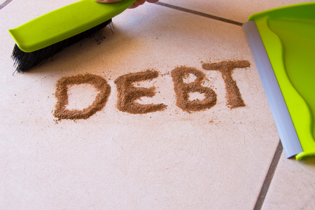 Help with debt concept with debt written in dirt on a floor and a person is about to sweep the debt dirt in a dust pan using a small hand broomの写真素材