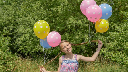 Cheerful and pretty girl with colorful balls attached to her hair and braids on her head. Funny idea with balloons.の写真素材