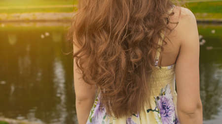 A girl with long, beautiful and curly hair against the backdrop of a pond in the park. Hair close-up. The girl sensually touches her hair. Youth. Beauty. Summer.の写真素材
