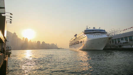 Cruise liner in Victoria harbor in the rays of sunset. View of the sea of Hong Kong and skyscrapers against the backdrop of the mountains.の写真素材
