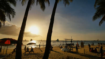 Beach with silhouettes of tourists among palm trees on the island of Boracay. Palm trees in the rays of sunset. Sailboats on the water. Philippine Tropics. Shooting in motion.の写真素材