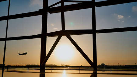 Silhouette of an airplane taking off at sunset at Beijing airport in the background of a window.の写真素材