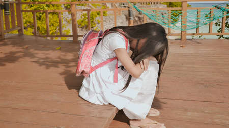 A philippine schoolgirl girl with a backpack is sitting and crying near the tropical coast. Sad mood.の写真素材