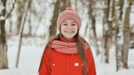 A teenage girl with freckles on her face happily smiles into the camera. A background of a winter...
