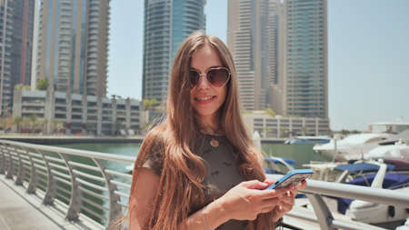 A girl with long hair dials a message on the smartphone at the quay of Dubai Marina.の写真素材