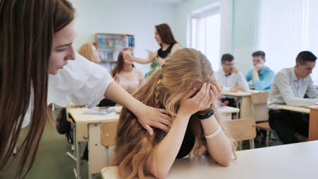 The girl is a schoolgirl crying in class and her classmates console her.の写真素材