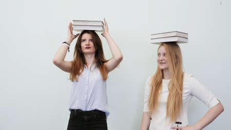 Two schoolgirls play with books holding them on their heads.の写真素材