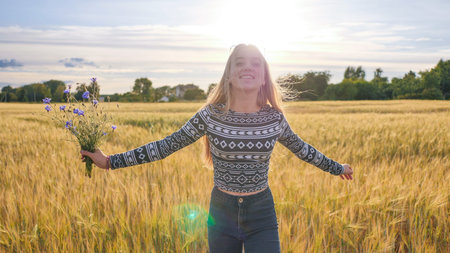 A sixteen year old teen girl with flowers of cornflowers is spinning in a field.の写真素材