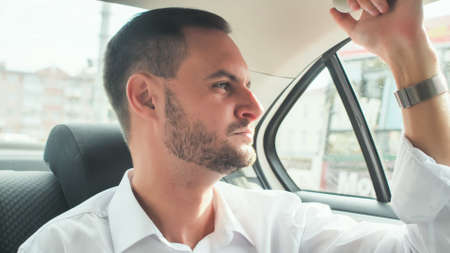 A young man with a beard rides in the back seat of the car.の写真素材