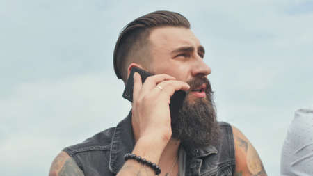 Brutal bearded man talking on the phone and smokes a cigarette.の写真素材