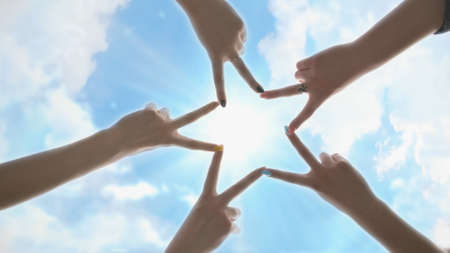 People forming star shape with their fingers against the blue sky with shining rays of the sun.の写真素材