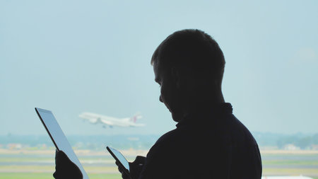 Silhouette of young men using tablet pc and phone on the background of an airplane taking off.