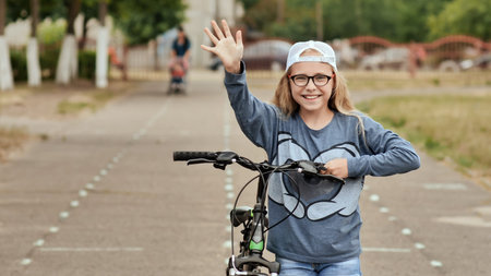 An eleven-year-old girl in a good mood rides a bicycle and after a stop shows a thumbs-up.