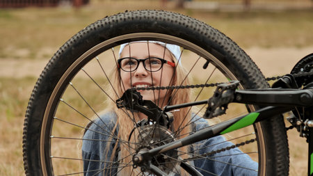An eleven-year-old girl twists and looks at the wheel of her bicycle.