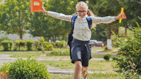 Happy eleven-year schoolgirl runs with a backpack after school.の写真素材
