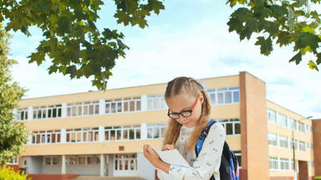 Little schoolgirl writes in a notebook against the background of her school.の写真素材