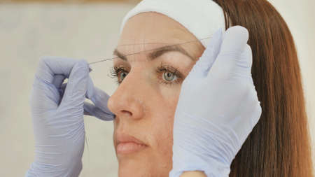 The girl beautician marks with the help of thread eyebrow tattoo. Permanent makeup. Permanent tattooing of eyebrows.の写真素材