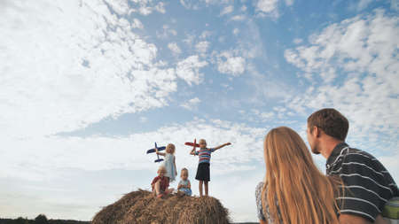 Children launch airplanes while standing on a stack of straw in front of their parents.の写真素材
