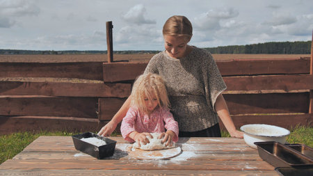 A little girl kneads the dough and her mother supports her. Homemade bread baking.の写真素材