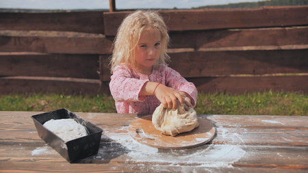 Little girl kneads the dough with her hands.
