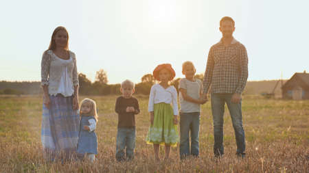 A large family goes on the field in the village during sunset.の写真素材