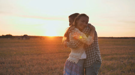 A guy is circling his girlfriend in his arms on a sunset background.