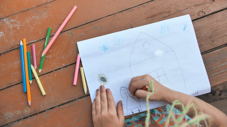 Child draws a pencil drawing of the house and his family. New home.