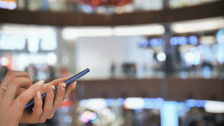 A girl in a shopping mall dials a message on the phone. Hands close up.