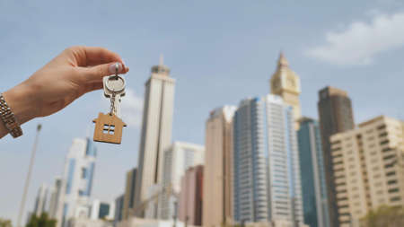 The concept of buying an apartment. Girl holds the keys to a new house against the backdrop of skyscrapers in the city.の写真素材