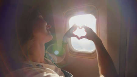 The girl at the airplanes porthole makes a heart out of her hands.の写真素材