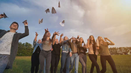 Happy friends launch paper airplanes at sunset.の写真素材