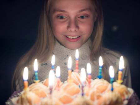 Teen girl admires burning candles at cake on her birthday.