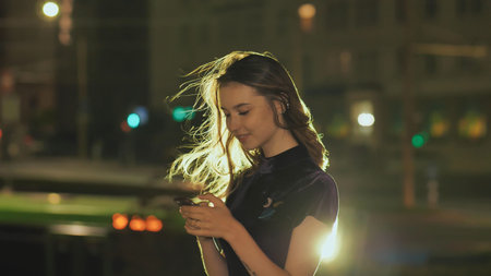 Portrait of young girl using smart phone and sending texts in night city.の写真素材
