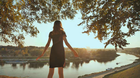 The girl enthusiastically runs to meet the sunset on the background of the city and raises her handsの写真素材