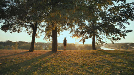 The girl enthusiastically runs to meet the sunset on the background of the city and raises her handsの写真素材